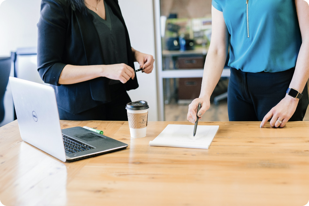 Zwei Frauen am Schreibtisch mit Laptop und Vertrag, diskutieren zum Third-Party Risk Management