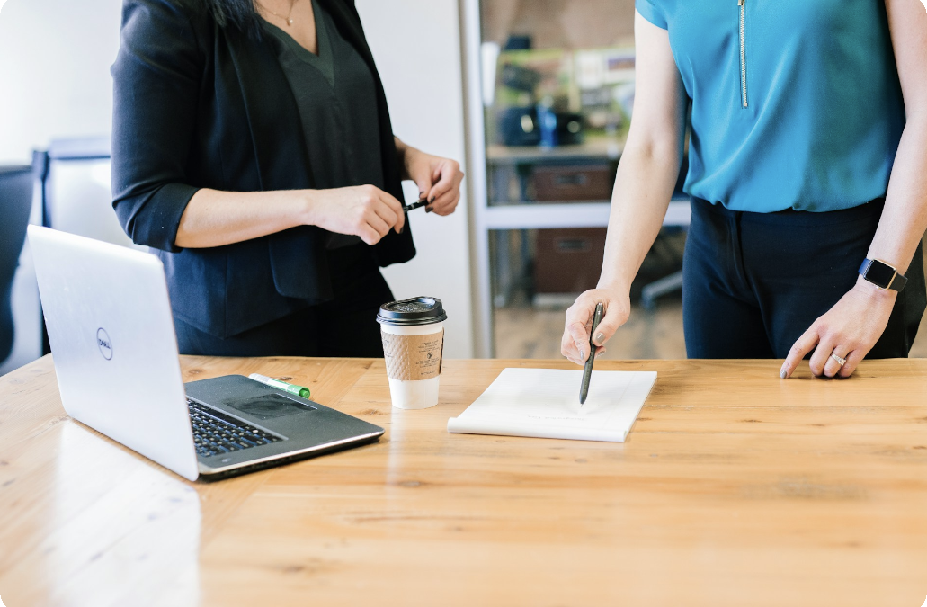 Zwei Frauen am Schreibtisch mit Laptop und Vertrag, diskutieren zum Third-Party Risk Management